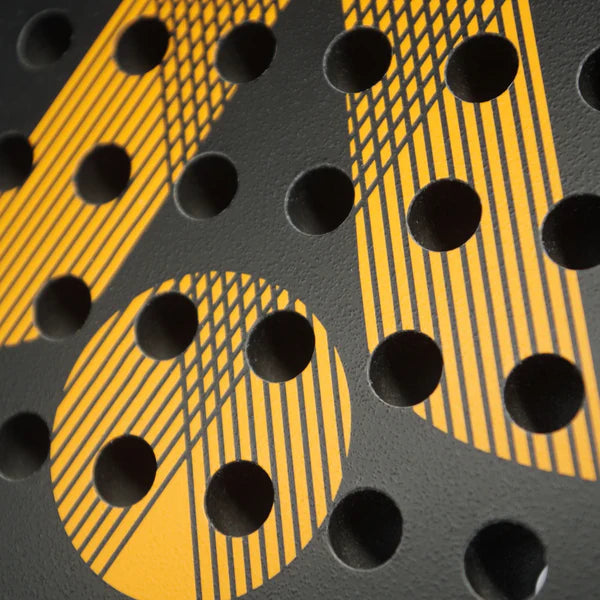 Close-up of the Karakal Air Lite 345 Padel - Orange by Karakal, showing its black surface with round holes and a bold yellow geometric pattern, characteristic of its lightweight graphite construction.