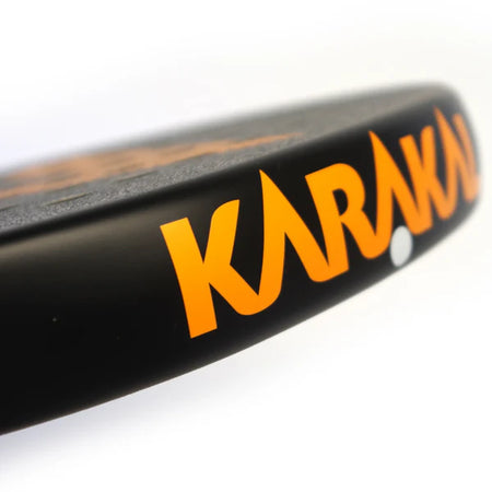 Close-up of the Karakal Air Lite 345 Padel - Orange, highlighting its lightweight graphite build and bold orange KARAKAL branding on the edge, set against a white background.