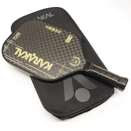 The Karakal Pure Touch Gold Pickleball Paddle, featuring a textured checkered surface with gold accents, rests atop its matching black zippered carrying case.