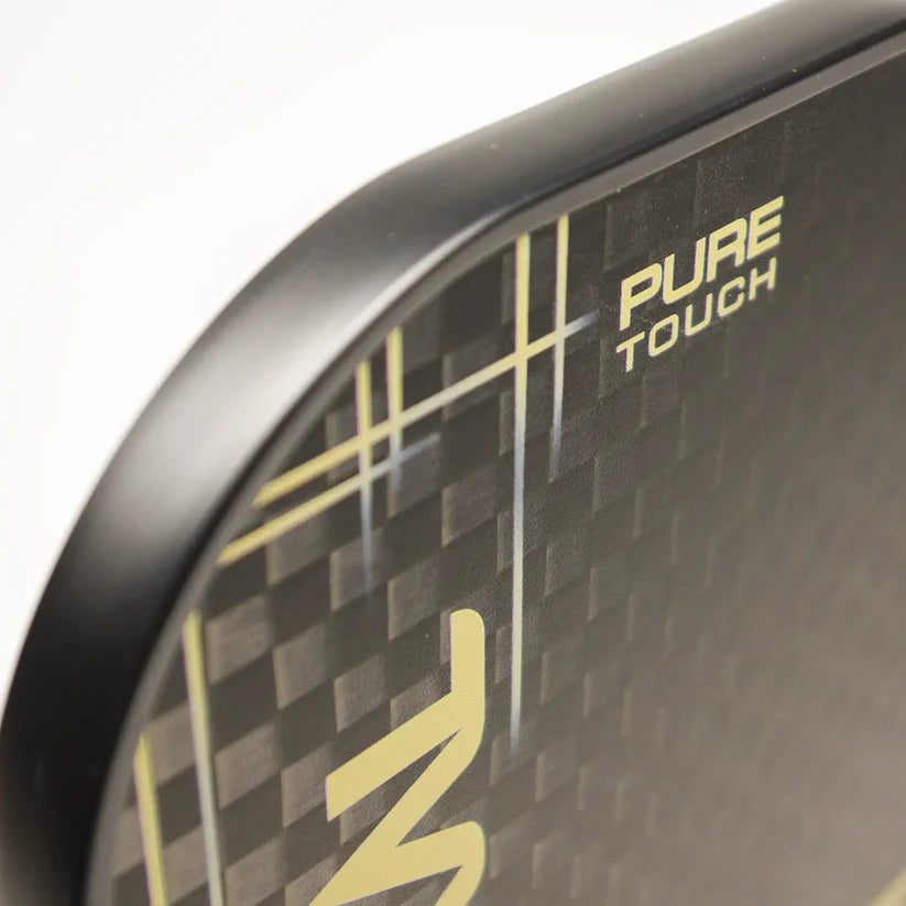 Close-up of the edge of a Karakal Pure Touch Gold Pickleball Paddle, featuring a black, carbon fiber-patterned surface with "PURE TOUCH" in yellow text. Brand: Karakal.