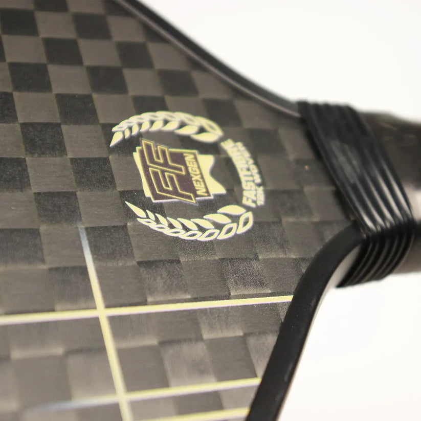 Close-up of the Karakal Pure Touch Gold Pickleball Paddle by Karakal, showcasing its textured carbon fiber surface with a checkerboard pattern and the FF Nexgen Fastfiner logo in a laurel wreath. The handle appears partially on the right.