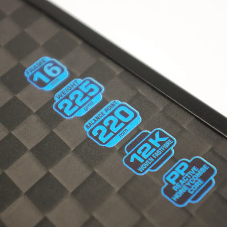Close-up of the Karakal Pure Touch Blue Pickleball Paddle’s black, checkered surface with blue specs: FRAME 16mm, WEIGHT 225g, BALANCE POINT 220mm, 12K WOVEN FABRIC, and PP REACTIVE HONEYCOMB POWER CORE. Brand: Karakal.