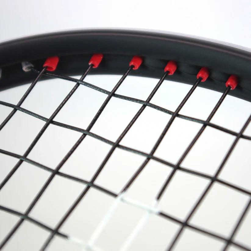 Close-up of the top section of the Karakal Air Power 2.1 Squash Racket by Karakal, featuring black strings threaded through red grommets on a high modulus graphite frame, set against a softly blurred white and gray background.