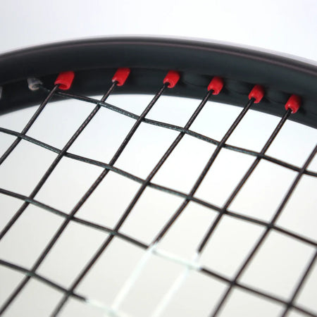 Close-up of the top section of the Karakal Air Power 2.1 Squash Racket by Karakal, featuring black strings threaded through red grommets on a high modulus graphite frame, set against a softly blurred white and gray background.
