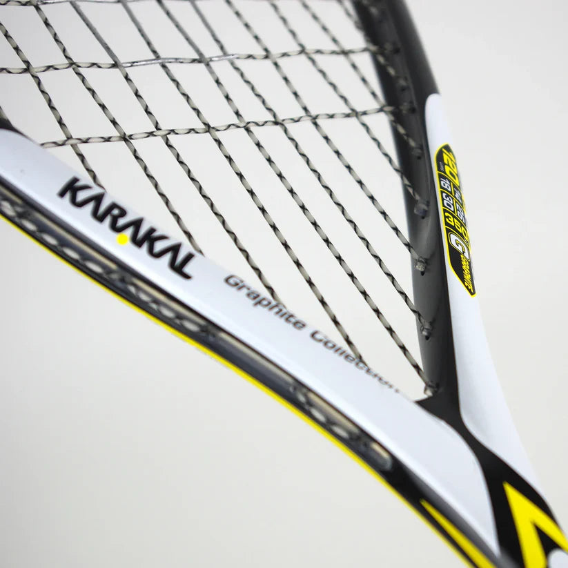 Close-up of the ultra-light Karakal Raw 120 2.1 Squash Racket, showing its strings and part of the white, black, and yellow frame with Karakal branding and graphics collection text visible.