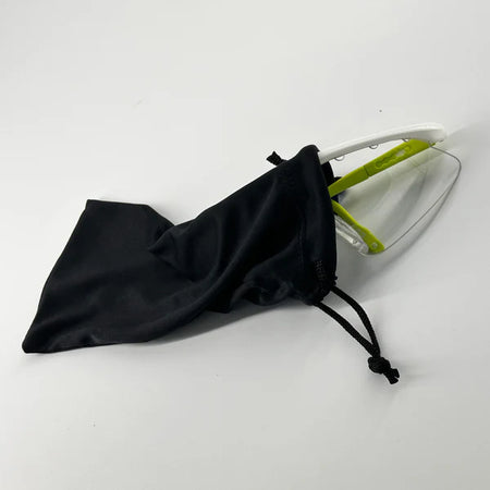 A pair of Karakal Pro 2500 Sports Eye Protection goggles for ladies/juniors, in green and white, partially tucked into a black Karakal pouch, resting on a white surface.