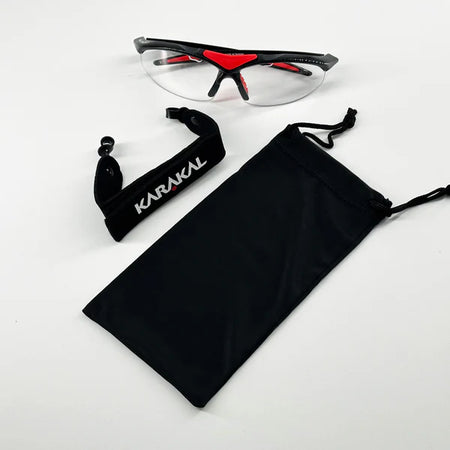 Karakal Adult Pro 3000 Sports Eye Protection by Karakal: clear safety glasses with black and red accents, anti-fog polycarbonate eye guards, adjustable black strap, and drawstring pouch. Displayed on a white background.
