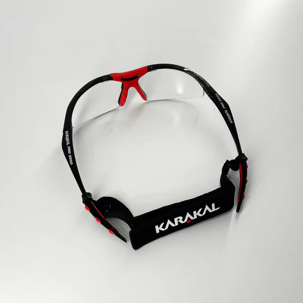 A pair of Karakal Adult Pro 3000 Sports Eye Protection goggles in black and red, featuring anti-fog polycarbonate eye guards and a black adjustable KARAKAL strap, displayed on a white surface.