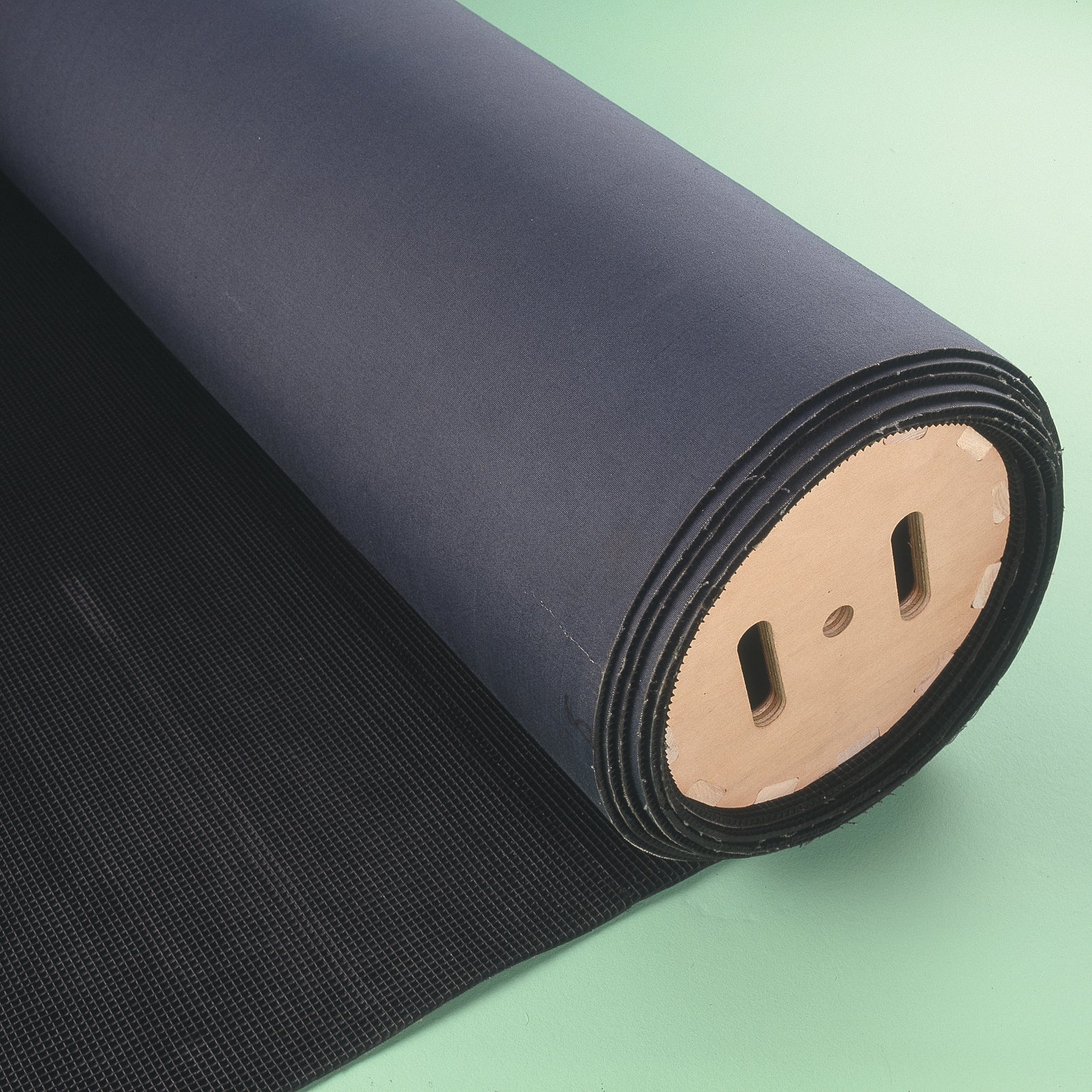 The Niels Larsen Matting Creel, a large black textured matting roll with a wooden core, is partially unrolled on a light green surface—ideal for efficient gymnastics mat storage.