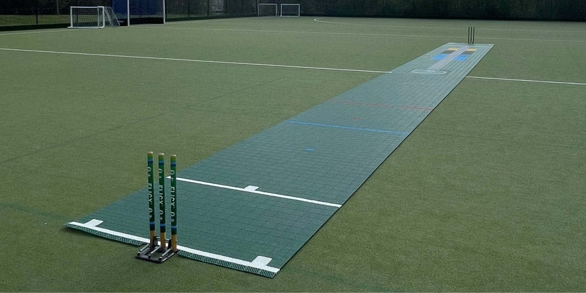 The Flicx 2G MAP (Multi Age Pitch) Match Cricket Pitch by Flicx UK is installed on an artificial turf field, creating a dedicated area for clubs and schools, complete with wickets at both ends and visible goals and fencing in the background.