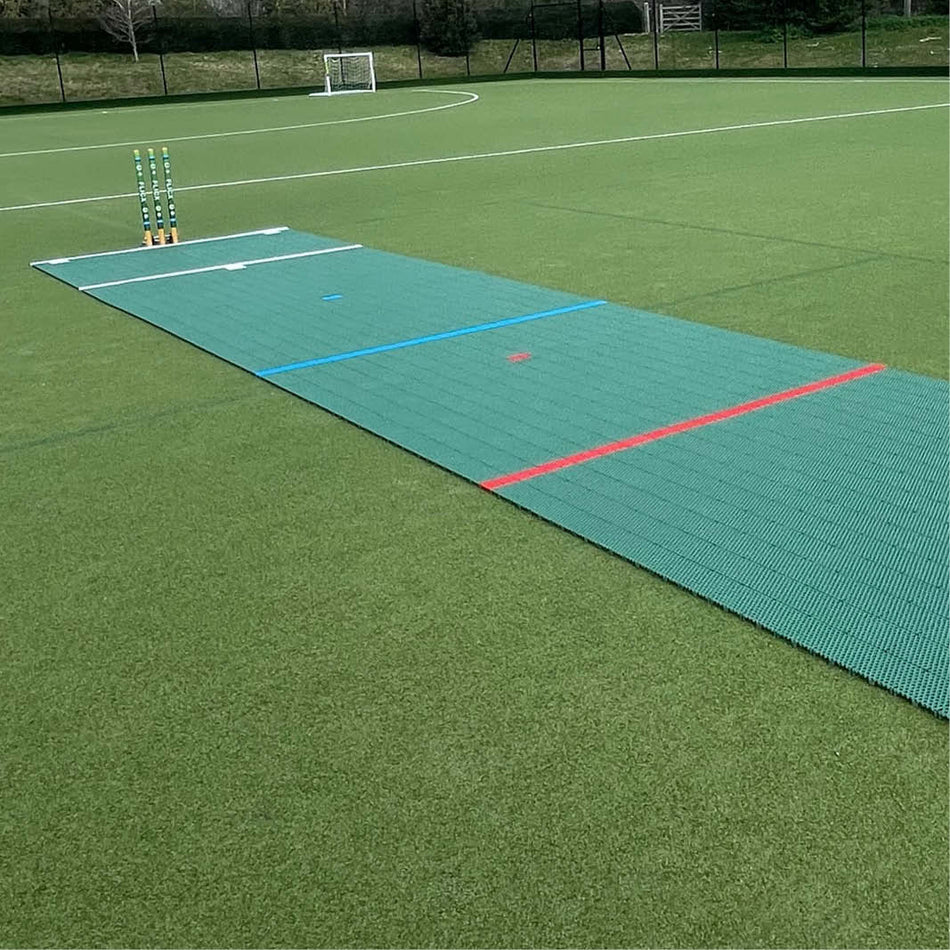 The Flicx 2G MAP (Multi Age Pitch) Match Cricket Pitch by Flicx UK is laid on green artificial turf, ideal for clubs and schools, with cricket stumps at one end and a small soccer goal behind the boundary fence.