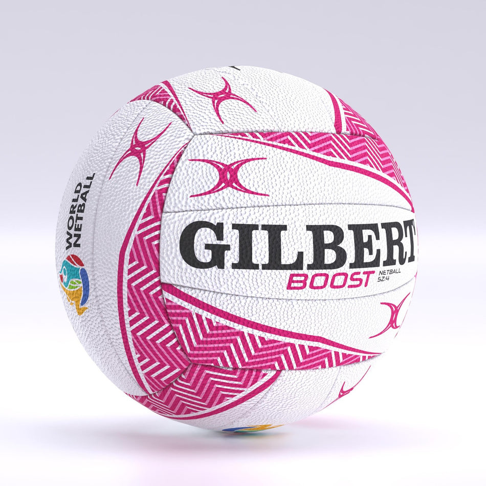 The Gilbert Boost Match Netball is a white size 5 ball featuring pink geometric patterns, bold black GILBERT branding, BOOST in pink, and a colorful World Netball logo. It has a design similar to Gilbert match balls and rugby balls.