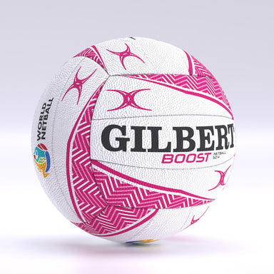 The Gilbert Boost Match Netball is a white size 5 ball featuring pink geometric patterns, bold black GILBERT branding, BOOST in pink, and a colorful World Netball logo. It has a design similar to Gilbert match balls and rugby balls.