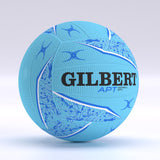 The Gilbert APT 2026 Netball is light blue with dark blue and white patterns, Duragrip texture for control, bold Gilbert branding, and smaller APT Netball text. The ball appears against a plain, light background.
