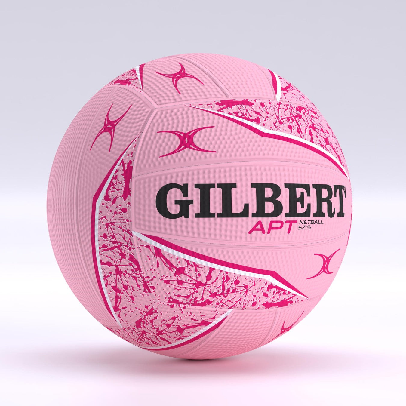 The Gilbert APT 2026 Netball features a pink design with abstract white and pink patterns, brand name and logo in black and red, plus a Duragrip surface ideal for outdoor play. Shown against a light, neutral backdrop.