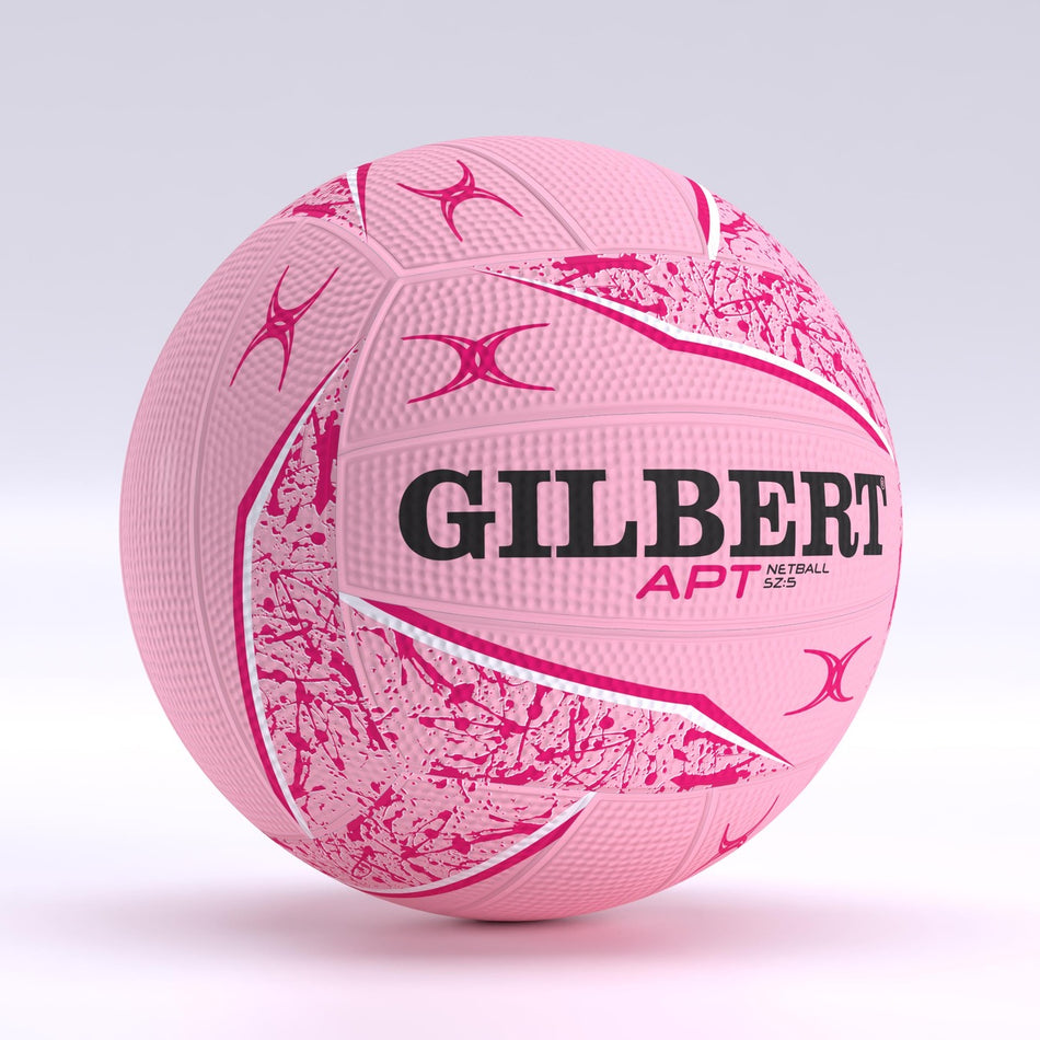 The Gilbert APT 2026 Netball features a pink design with abstract white and pink patterns, brand name and logo in black and red, plus a Duragrip surface ideal for outdoor play. Shown against a light, neutral backdrop.