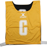 The Gilbert Reversible Netball Bibs in amber/black feature a large white "C", the GILBERT logo above it, and adjustable white straps—ideal for team or individual use in matches.