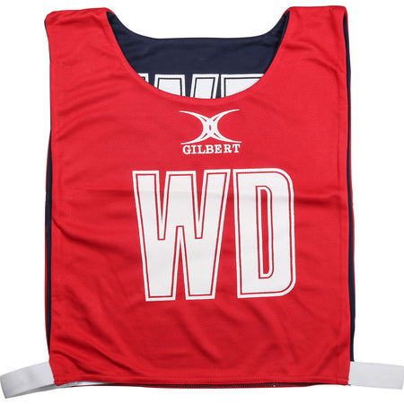 The Gilbert Reversible Netball Bibs in red/navy feature the GILBERT logo and large white WD letters on the front, with white hook-and-loop side straps for easy fitting—perfect for any netball bib collection.