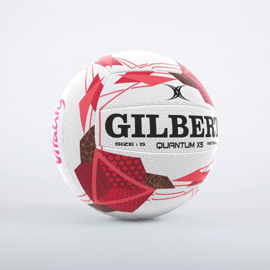 The Gilbert Quantum X5 England Netball SZ5 is a white netball with red and pink geometric patterns, black text, and partial "Vitality" branding, shown against a plain light grey background.