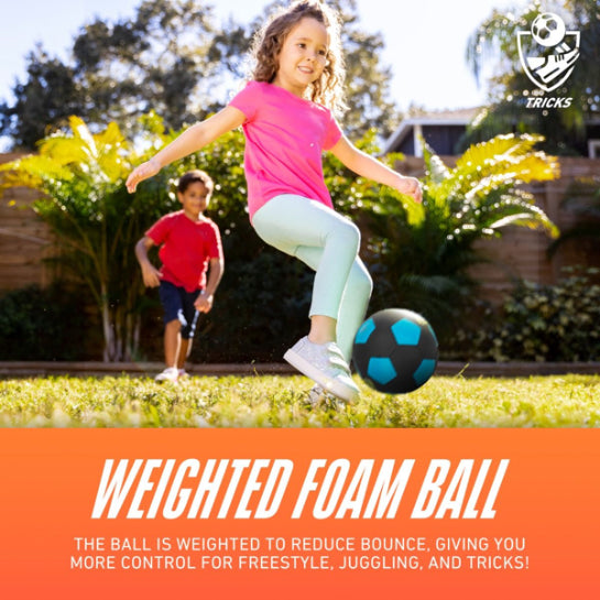A smiling young girl kicks a Nerf Freestyle Soccer Ball by Nerf, featuring blue and black colors, on a grassy lawn while a boy in a red shirt runs behind her. Text reads, “Weighted Foam Ball—reduced bounce for better control.”.