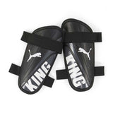 The Puma King Strap Shin Guard by Puma offers premium protection for soccer players, featuring "KING" in white and white Puma logos on black guards secured with black elastic straps.
