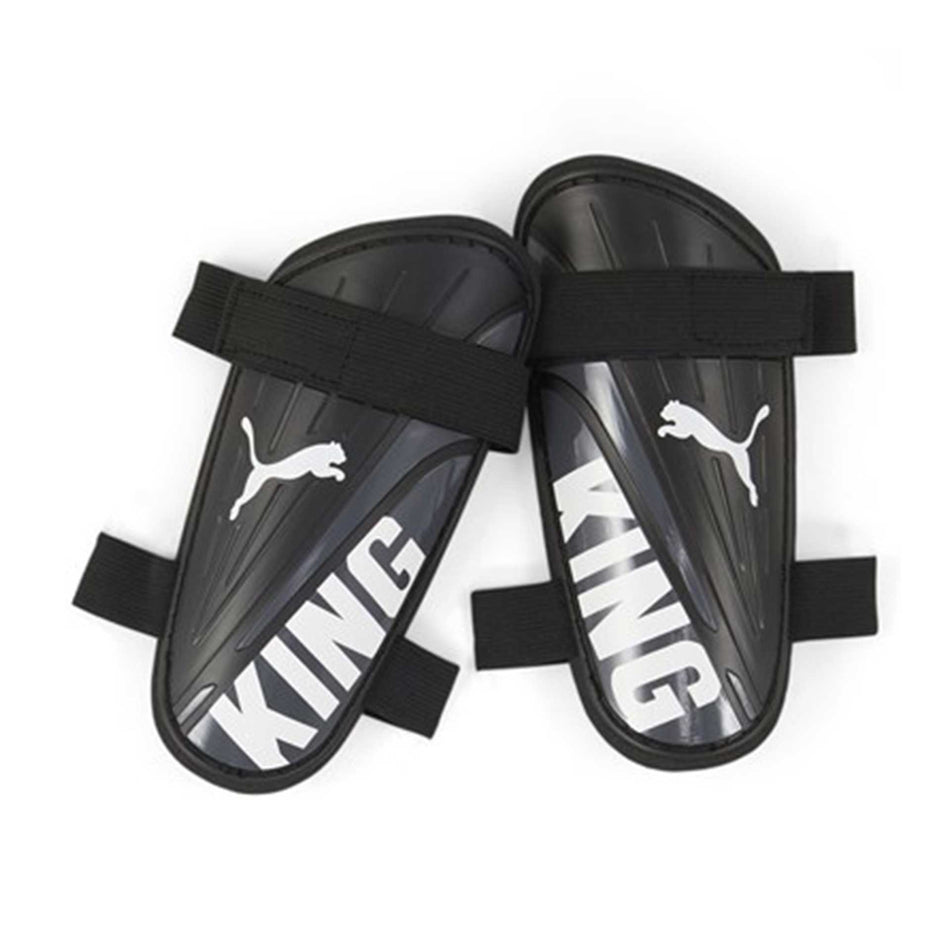 The Puma King Strap Shin Guard by Puma features black guards with white logos and "KING" text, plus black elastic straps for a secure fit, delivering reliable shin protection during soccer matches.