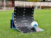A soccer ball strikes the Precision Training PrecisionPLAY Skills Trainer Ramp Rebounder on green artificial turf, with a goalpost and fencing in the background.