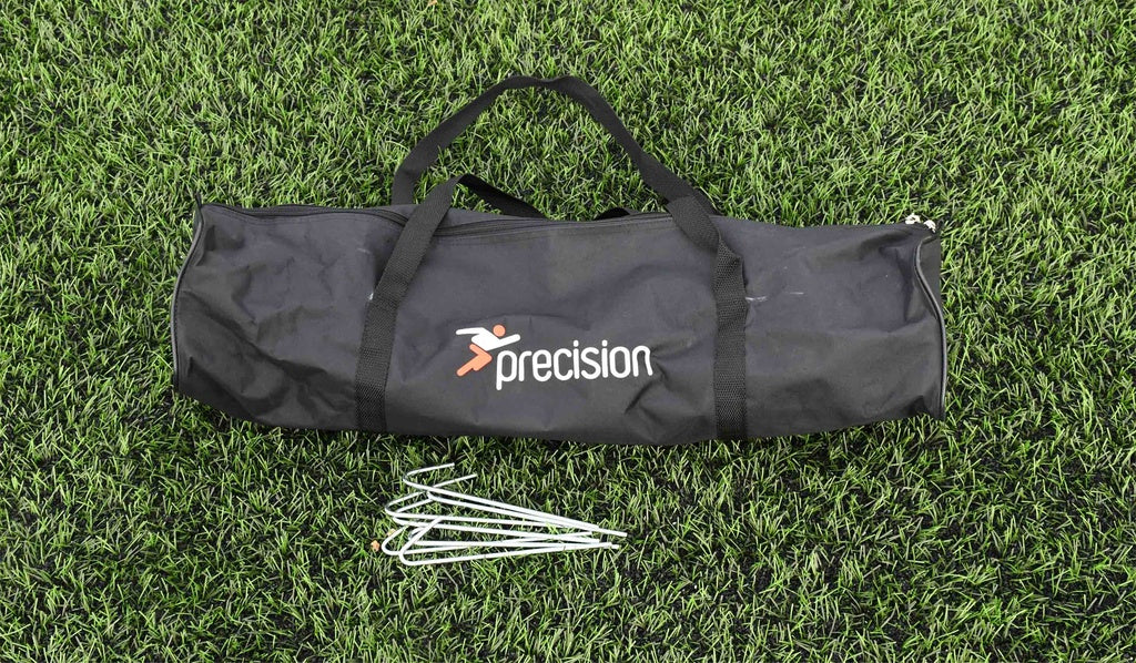A black Precision Training sports bag rests on green artificial grass with four metal ground stakes—perfect for first touch drills or assembling the Precision Mini Foot Tennis Set for skill training.