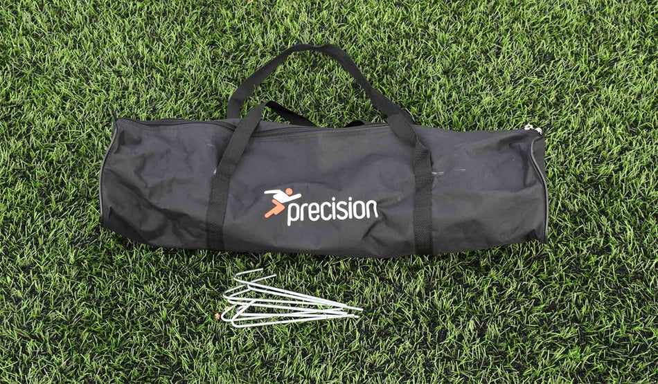 A black Precision Training sports bag rests on green artificial grass with four metal ground stakes—perfect for first touch drills or assembling the Precision Mini Foot Tennis Set for skill training.