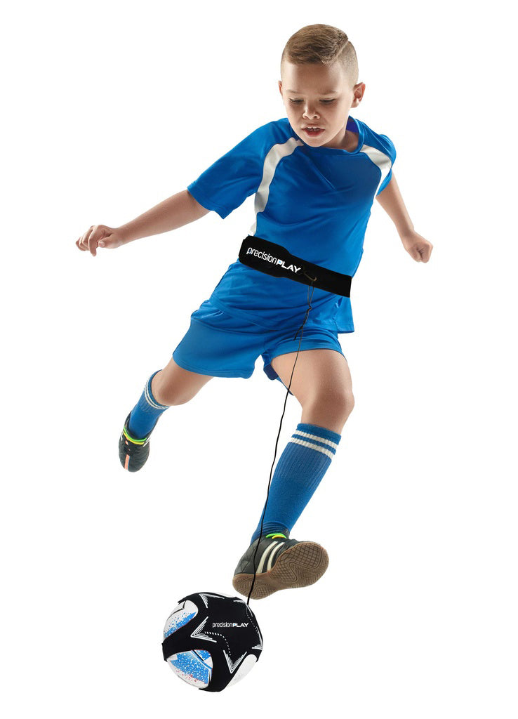 A young boy in a blue soccer uniform uses the Precision Training PrecisionPLAY Solo Kick Skills Trainer, kicking a black and white soccer ball attached to his waist with a cord, against a white background.