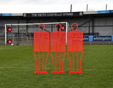 A Precision Training Precision Pro Club Mannequin (Single) in red stands on a grassy field by the goalpost—perfect for free kick drills—with empty stands and the sign "THE KEITH COSTELLO STAND" visible in the background.