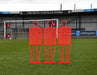 A Precision Training Precision Pro Club Mannequin (Single) in red stands on a grassy field by the goalpost—perfect for free kick drills—with empty stands and the sign "THE KEITH COSTELLO STAND" visible in the background.