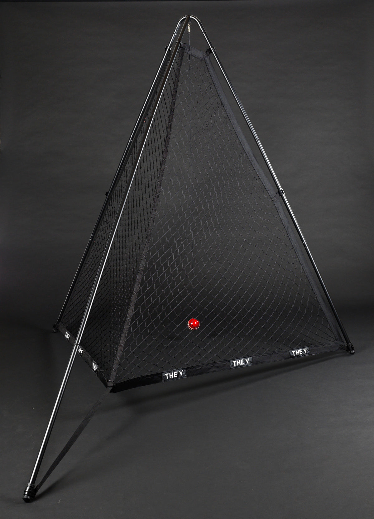 A pyramid-shaped The V Pro 2.0 cricket training net by The V with a black frame stands on a dark background. A single red ball is inside, and THE V is written in white on the base—ideal for improving your batting skills during practice.