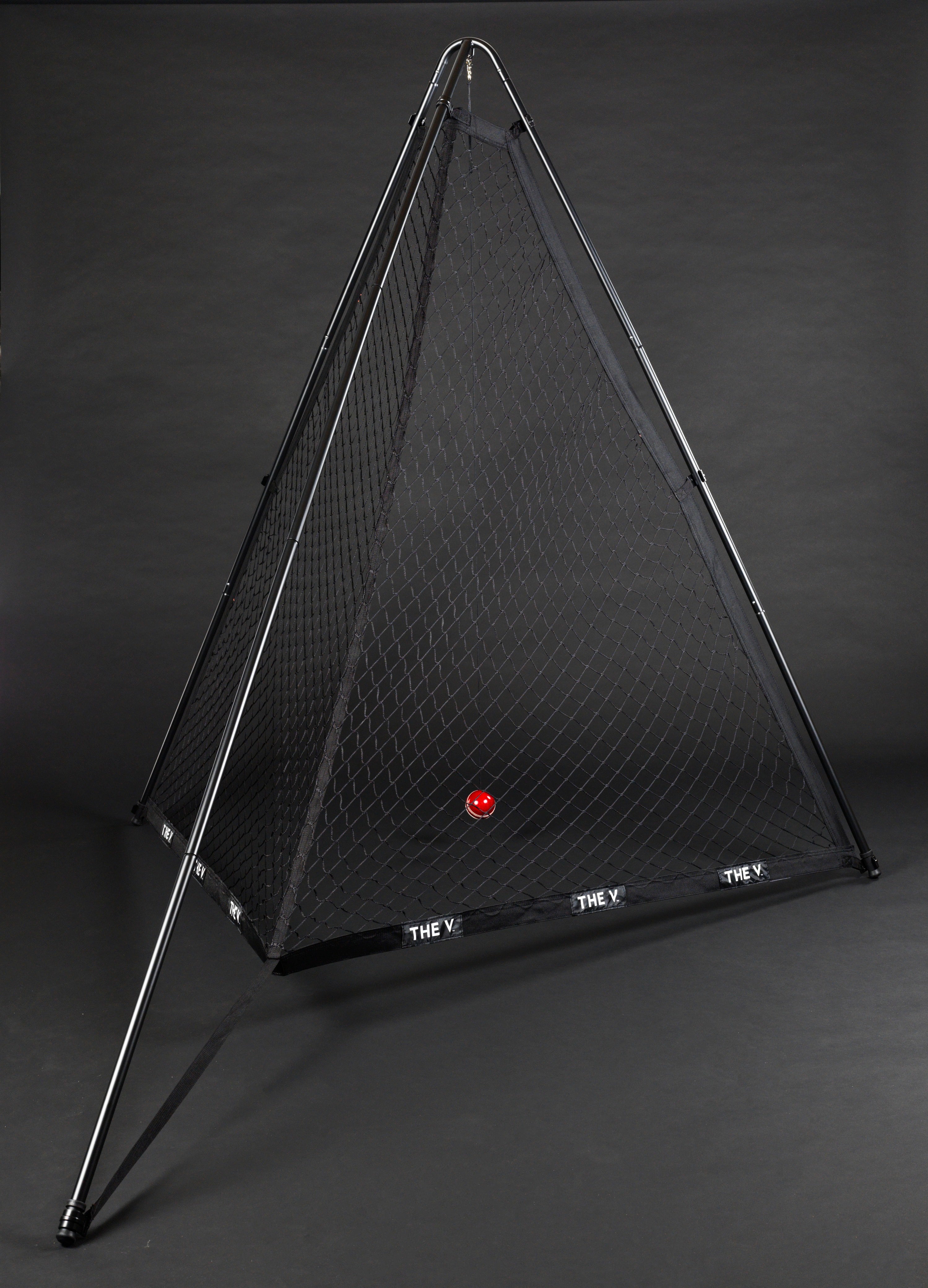 A pyramid-shaped The V Pro 2.0 cricket training net by The V with a black frame stands on a dark background. A single red ball is inside, and THE V is written in white on the base—ideal for improving your batting skills during practice.
