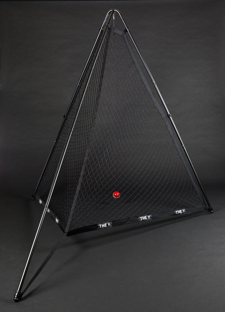 A pyramid-shaped The V Pro 2.0 cricket training net by The V with a black frame stands on a dark background. A single red ball is inside, and THE V is written in white on the base—ideal for improving your batting skills during practice.