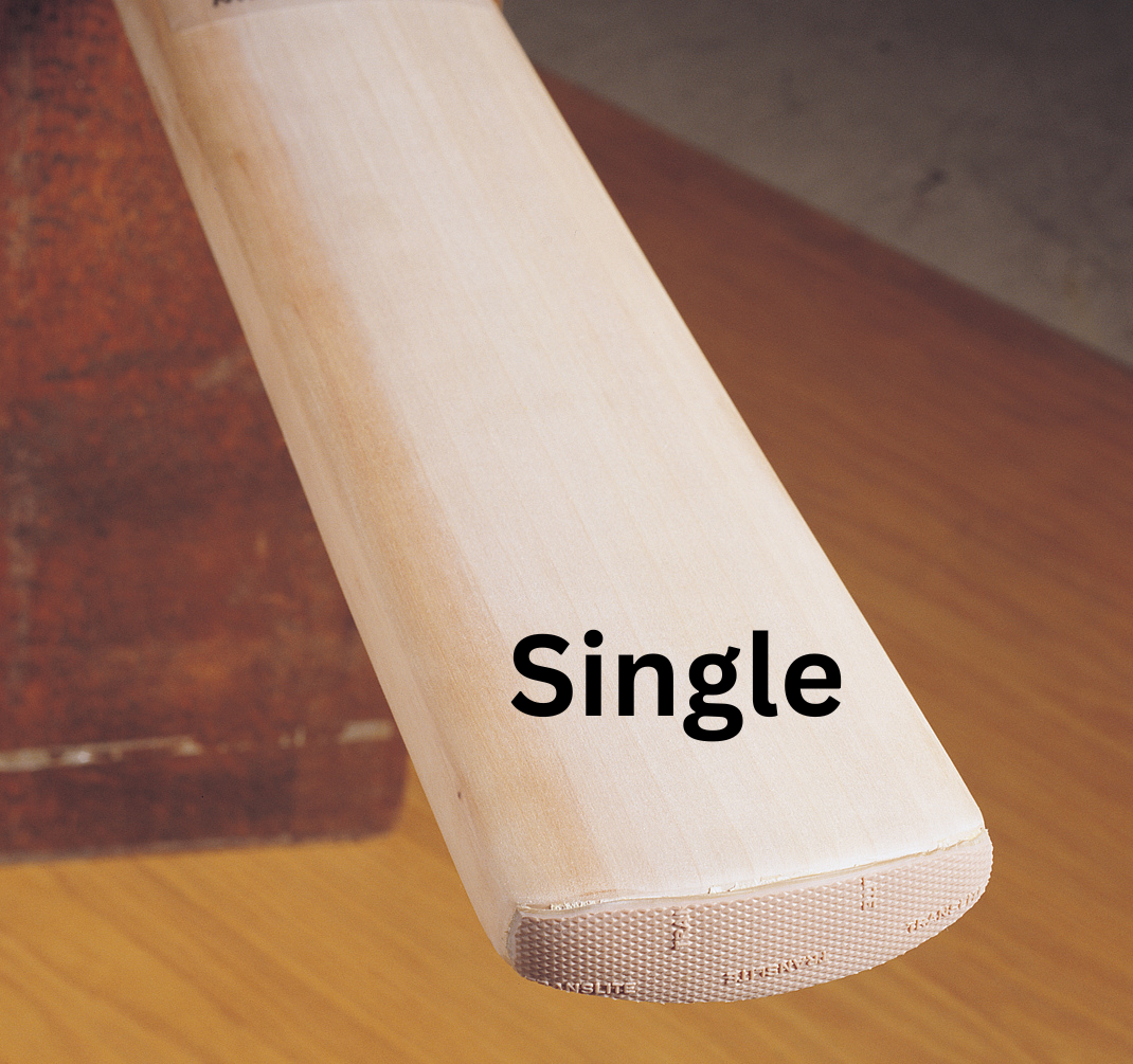 Close-up of a Gray Nicolls cricket bat with "Single" printed in bold black letters on the blade, featuring the Gray-Nicolls Protectoe toe guard for extra protection, resting on a wooden surface.