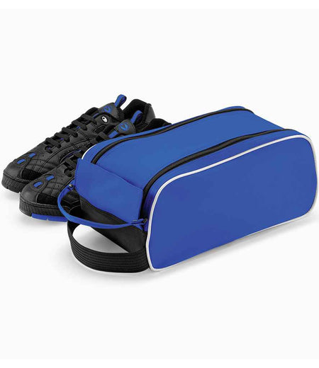 A pair of black athletic shoes with blue accents sits behind the Quadra Teamwear Shoe Bag by Quadra, a blue zippered bag with a webbing carry handle and white trim, all displayed on a plain white background.