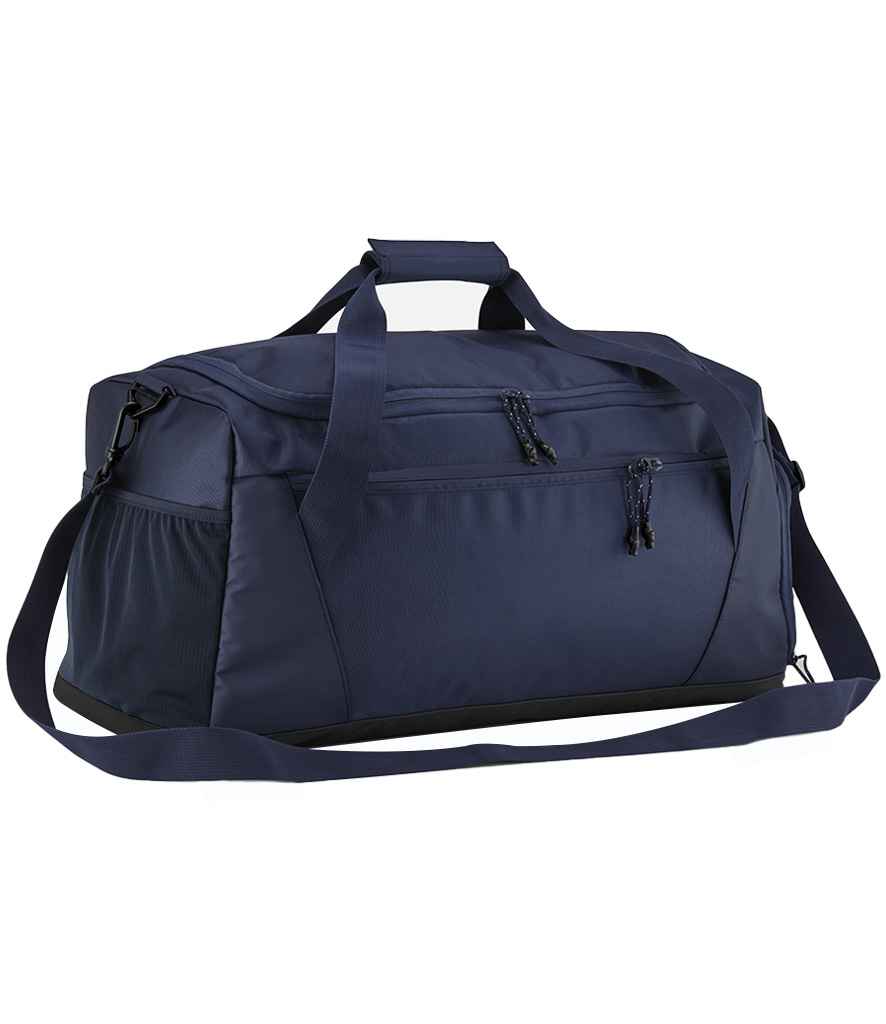 The Quadra Multi-Sport Locker Holdall by Quadra is a navy duffel bag made from recycled polyester, featuring a top handle, adjustable shoulder strap, side pocket, front zippered compartments, and a dedicated racquet pocket on a white background.