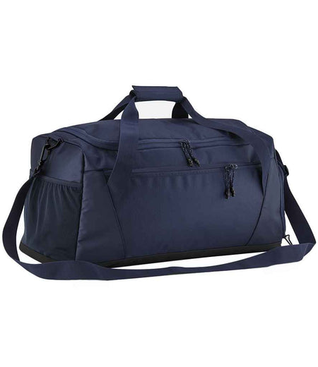 The Quadra Multi-Sport Locker Holdall by Quadra is a navy duffel bag made from recycled polyester, featuring a top handle, adjustable shoulder strap, side pocket, front zippered compartments, and a dedicated racquet pocket on a white background.