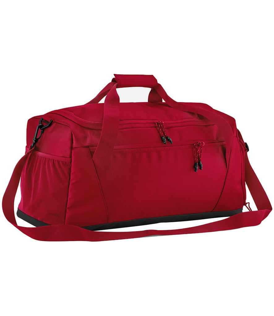 The Quadra Multi-Sport Locker Holdall by Quadra, in red recycled polyester, features an adjustable shoulder strap, two handles, a front zip pocket, and a side mesh pocket, shown on a plain white background.
