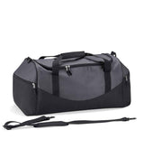 The Quadra Teamwear Holdall by Quadra is a large grey/black/black duffel bag with side pockets, top handles featuring a padded grip, and a detachable shoulder strap shown in front of the bag on a white background.