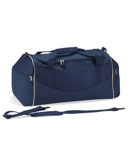 The Quadra Teamwear Holdall by Quadra in Navy/Navy/Putty features zippered pockets, white piping, two padded handles, and a detachable shoulder strap placed in front.
