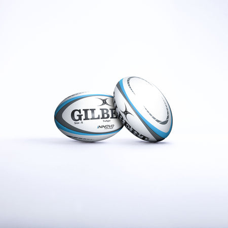 Two Gilbert Innovo Match Balls (Size 5) by Gilbert, white and blue, are displayed on a plain white background—one upright and one lying on its side with the logo clearly visible.