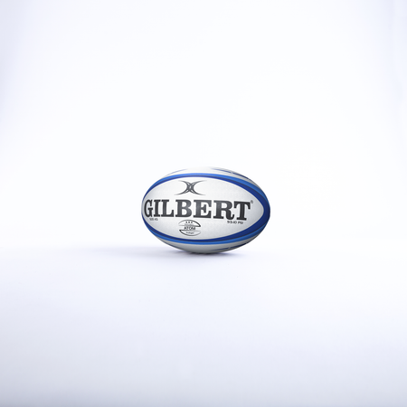 The Gilbert Atom Match Ball, in white and blue, stands upright on a plain white background, reflecting the renowned quality of Gilbert rugby balls.