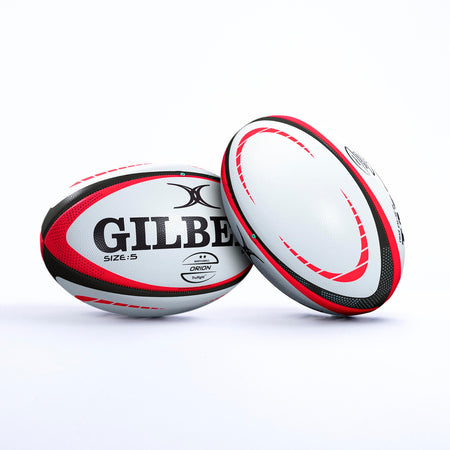 Two white Gilbert Orion Match Rugby Balls, hand stitched with red and black patterns, display the Gilbert brand, World Rugby logo, and size 5 label. Set on a plain white background, one ball is upright while the other leans against it.