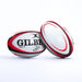 Two white Gilbert Orion Match Rugby Balls, hand stitched with red and black patterns, display the Gilbert brand, World Rugby logo, and size 5 label. Set on a plain white background, one ball is upright while the other leans against it.