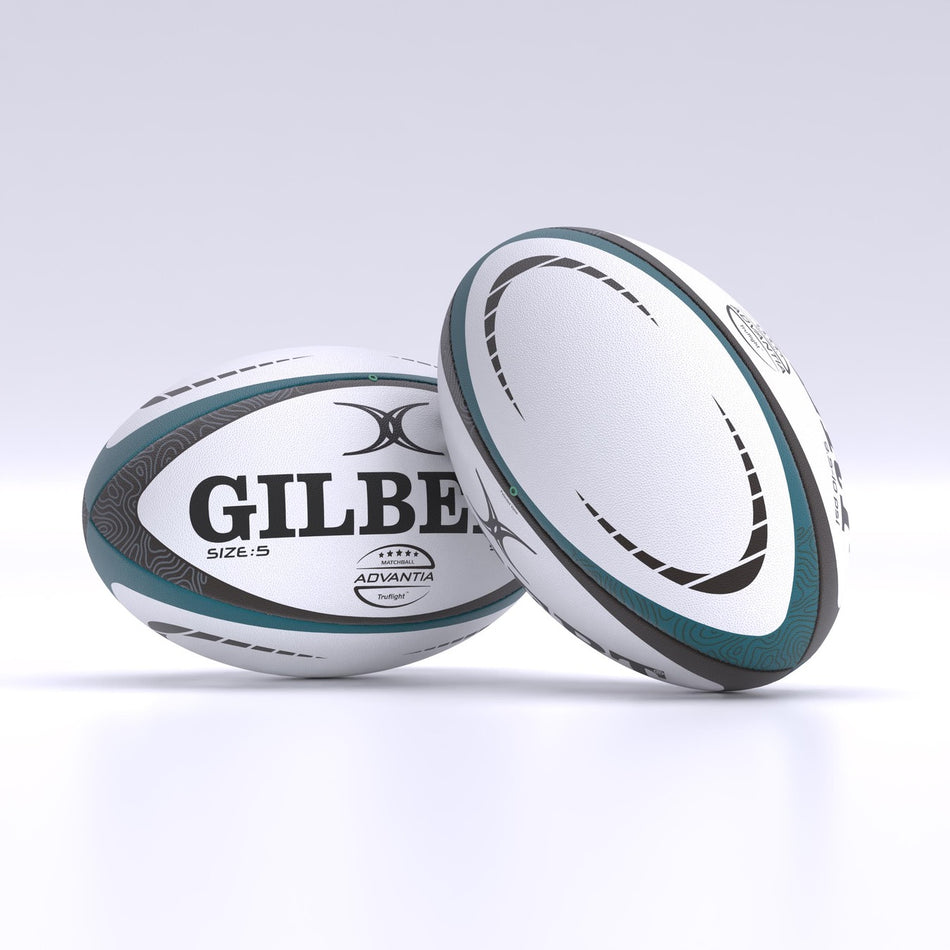 Two white and teal Gilbert Advantia Match Rugby Balls with black and gray patterns rest on a white surface. One hand-stitched ball lies flat, showing the Gilbert name, while the other stands upright, displaying its side.