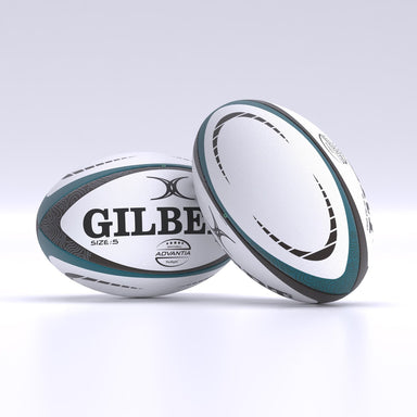 Two white and teal Gilbert Advantia Match Rugby Balls with black and gray patterns rest on a white surface. One hand-stitched ball lies flat, showing the Gilbert name, while the other stands upright, displaying its side.