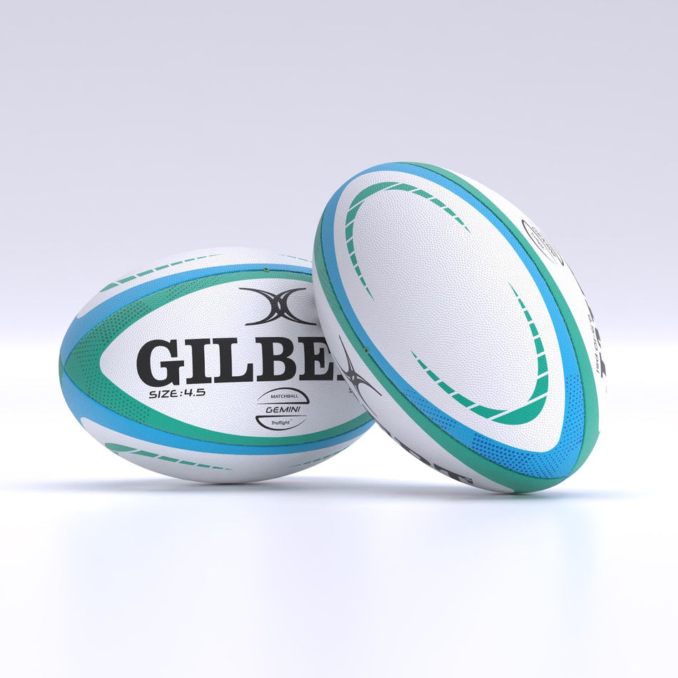 Two white Gilbert Gemini Match Rugby Balls by Gilbert, hand-stitched for durability, feature green and blue curved patterns. One stands upright while the other leans on a light surface. Perfect for skill development or as a Size 4.5 match ball.