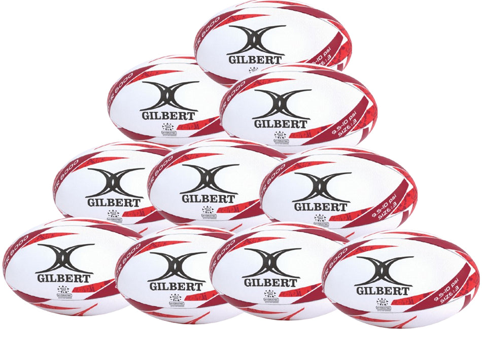 Ten Gilbert G-TR6000 Training Rugby Balls from Gilbert, featuring a durable rubber surface, white color with red accents, are stacked in a pyramid. This is the Gilbert G-TR6000 Training Rugby Ball Ten Pack.